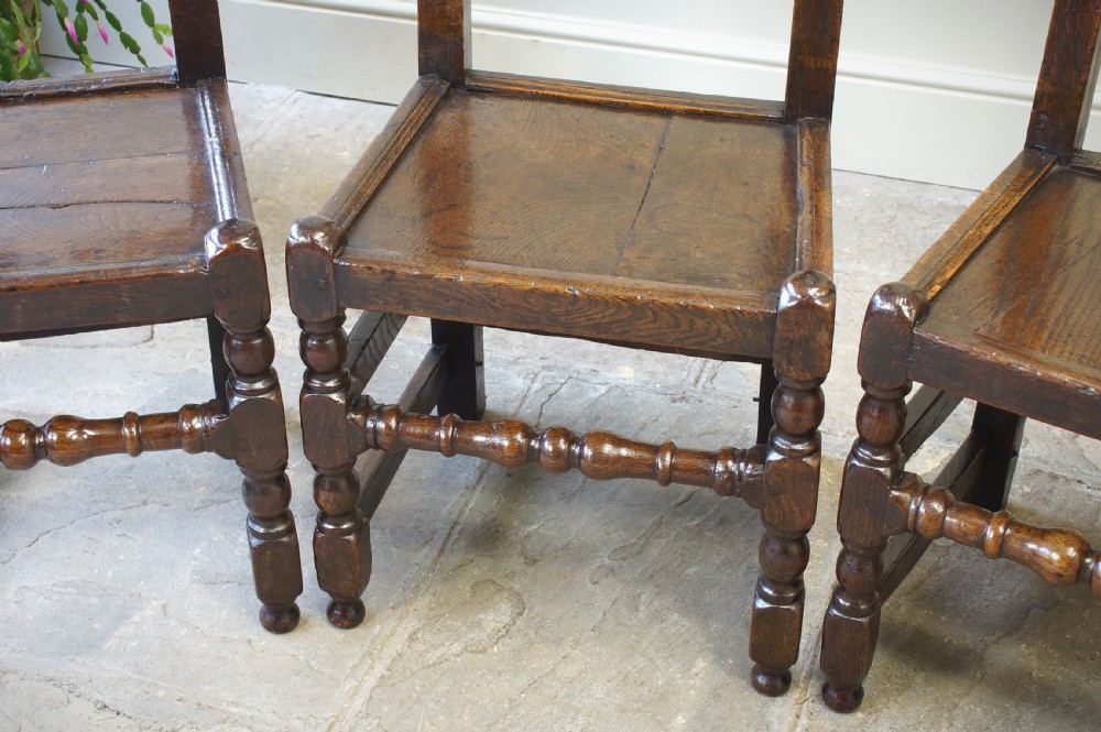 Set of four 17th-century carved dark oak backstool chairs featuring openwork carved cresting rails, turned stretchers, and solid wooden panel seats. View VI