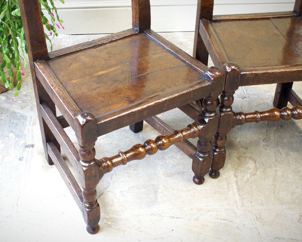Set of four 17th-century carved dark oak backstool chairs featuring openwork carved cresting rails, turned stretchers, and solid wooden panel seats. View VIII