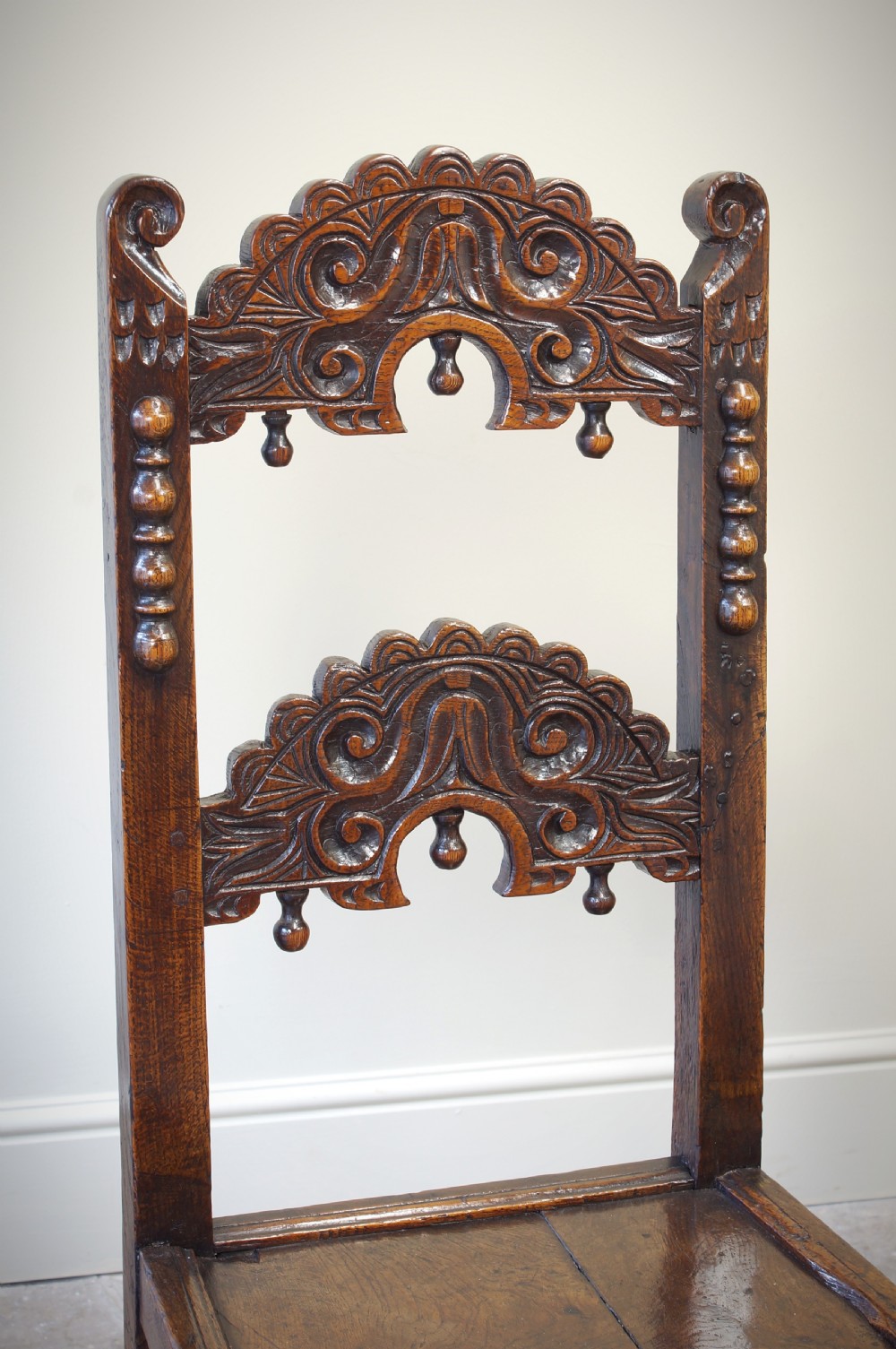 Set of four 17th-century carved dark oak backstool chairs featuring openwork carved cresting rails, turned stretchers, and solid wooden panel seats. View IX