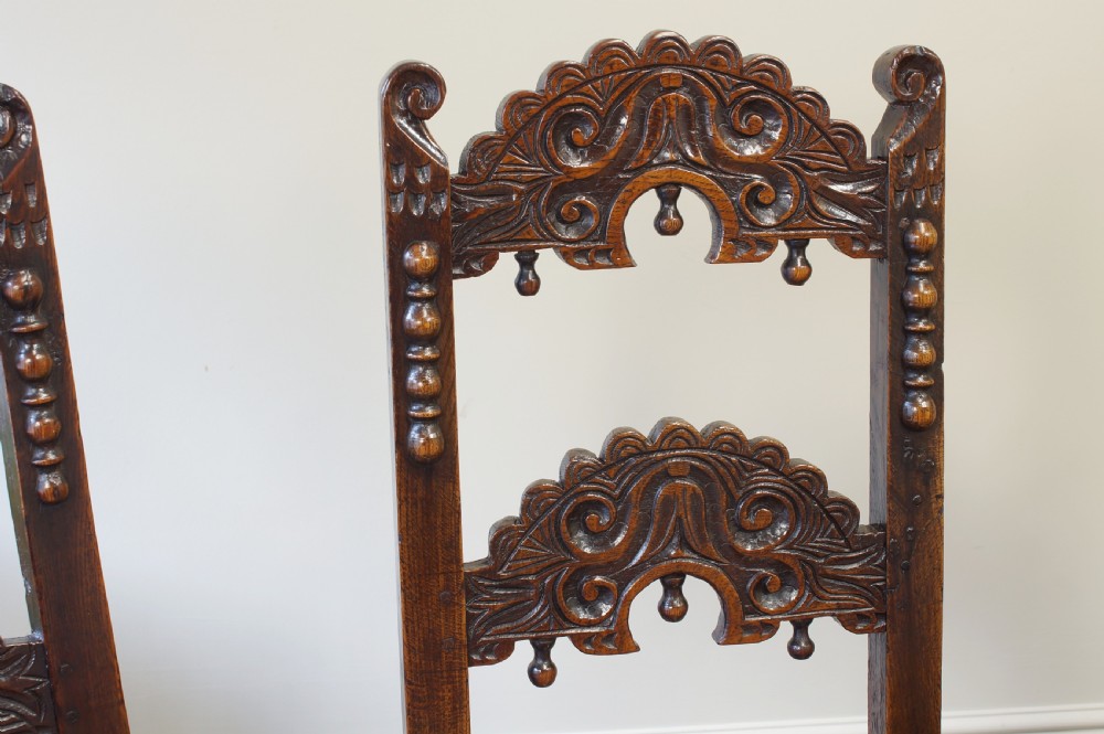 Set of four 17th-century carved dark oak backstool chairs featuring openwork carved cresting rails, turned stretchers, and solid wooden panel seats. View X