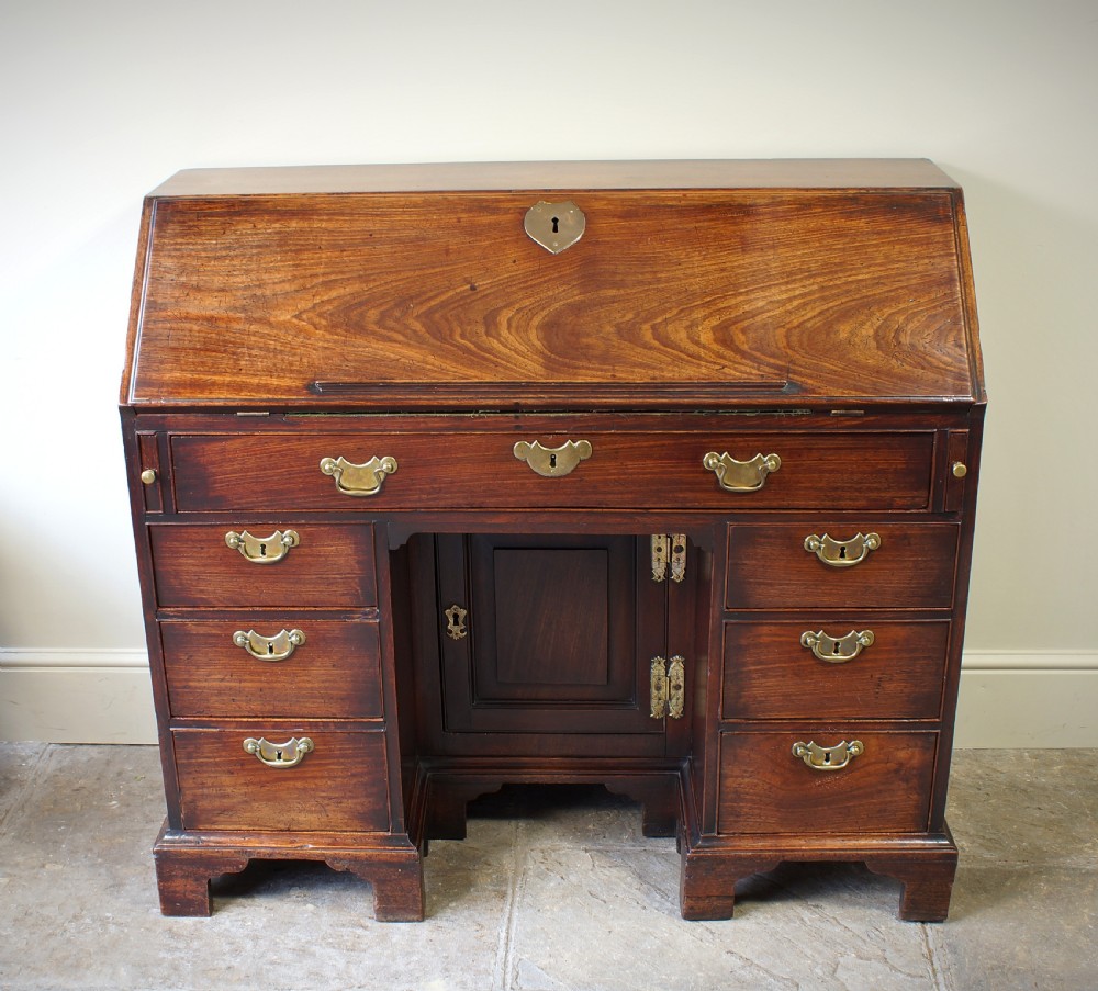 An early Georgian mahogany kneehole bureau featuring a slanted fall-front top lid, brass drop handles, multiple drawers, and a central recessed cupboard on bracket feet. View II