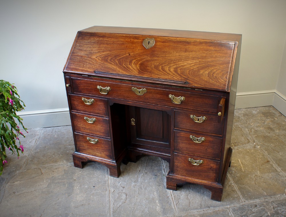 An early Georgian mahogany kneehole bureau featuring a slanted fall-front top lid, brass drop handles, multiple drawers, and a central recessed cupboard on bracket feet. View VII