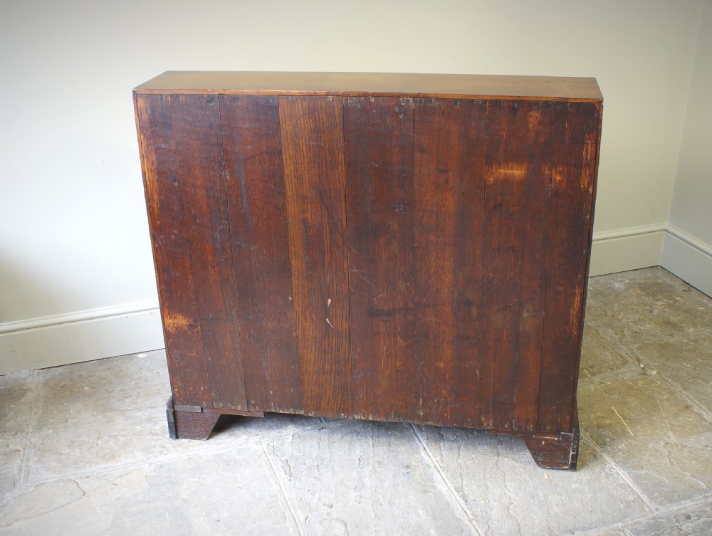 An early Georgian mahogany kneehole bureau featuring a slanted fall-front top lid, brass drop handles, multiple drawers, and a central recessed cupboard on bracket feet. View XIII