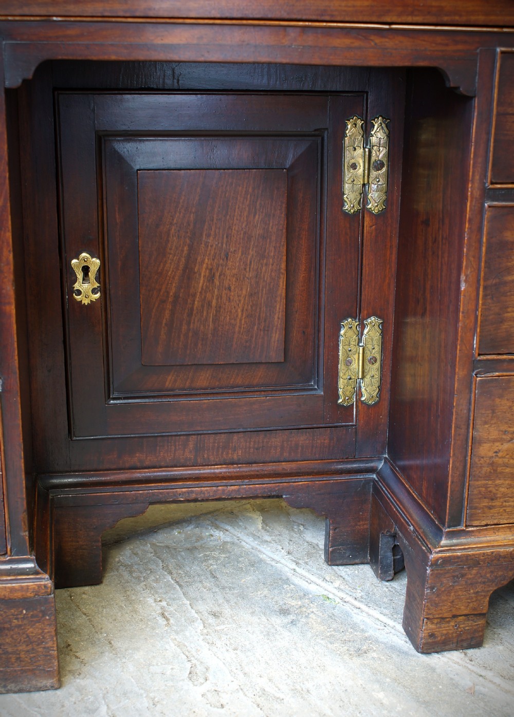 An early Georgian mahogany kneehole bureau featuring a slanted fall-front top lid, brass drop handles, multiple drawers, and a central recessed cupboard on bracket feet. View XVI