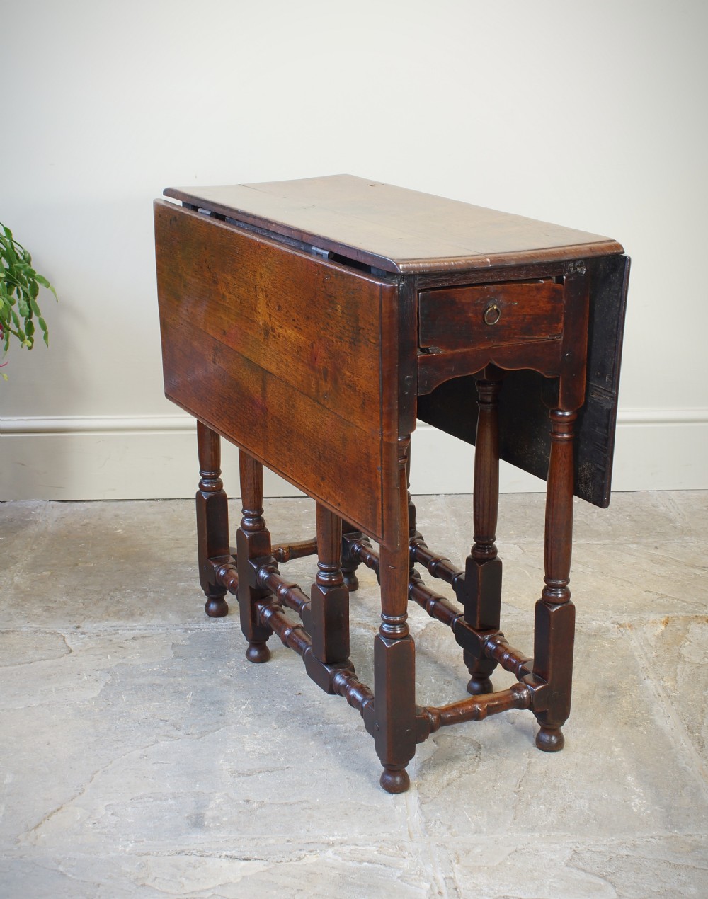 An antique late 17th-century walnut gateleg table featuring turned legs, stretchers, a single frieze drawer, and two hinged drop leaves. View V