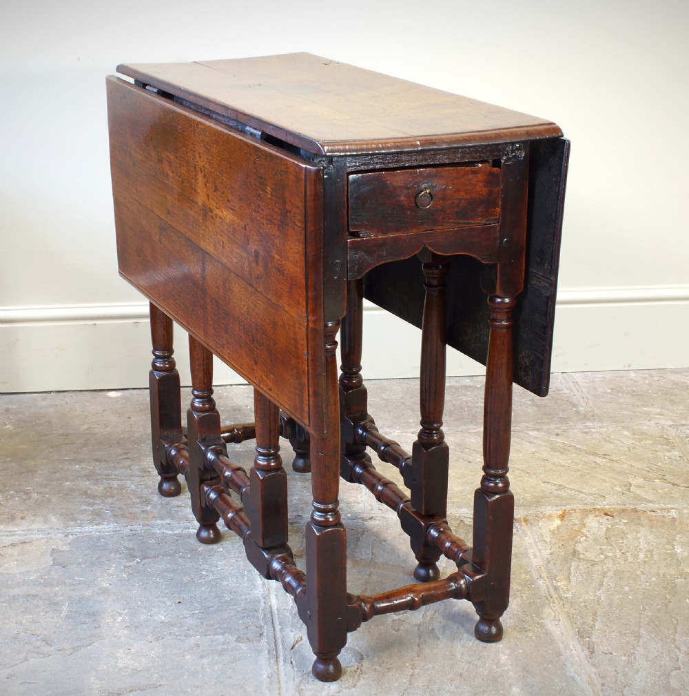 An antique late 17th-century walnut gateleg table featuring turned legs, stretchers, a single frieze drawer, and two hinged drop leaves. View VI