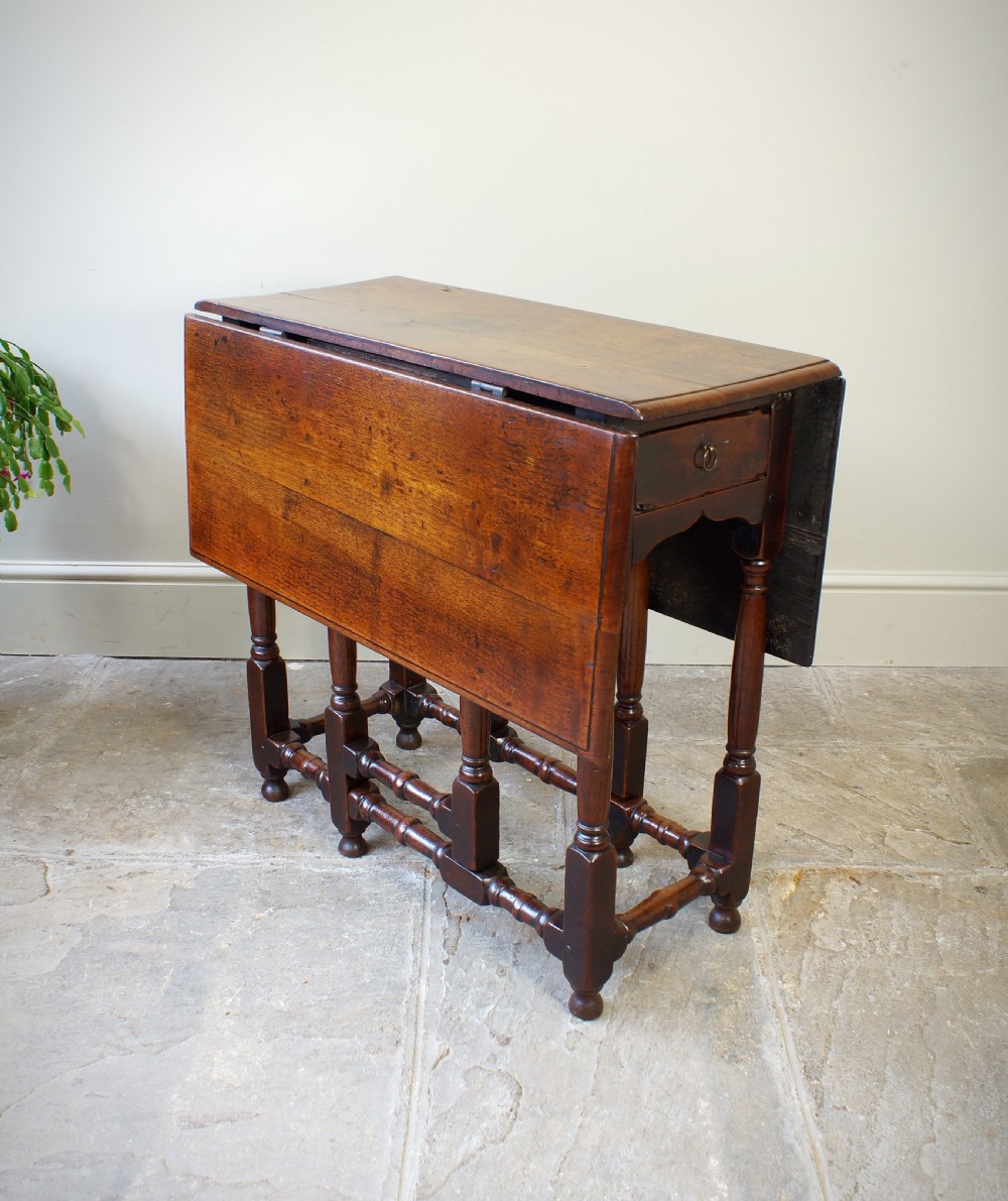 An antique late 17th-century walnut gateleg table featuring turned legs, stretchers, a single frieze drawer, and two hinged drop leaves. View VII