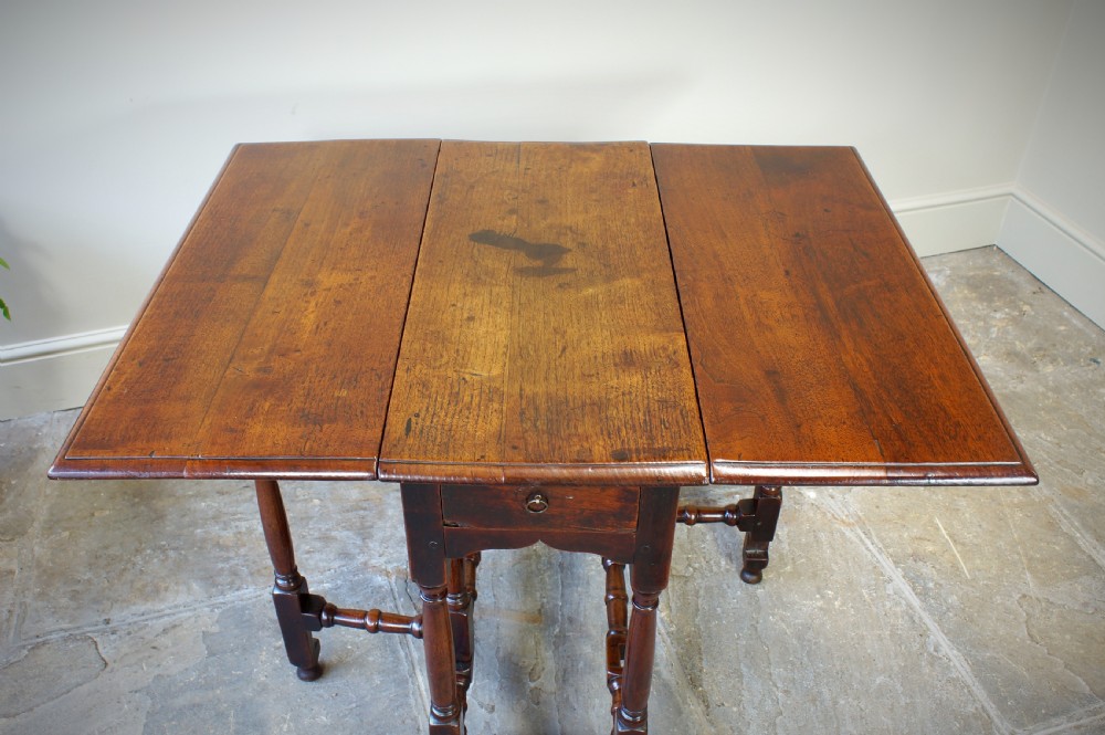 An antique late 17th-century walnut gateleg table featuring turned legs, stretchers, a single frieze drawer, and two hinged drop leaves. View IX