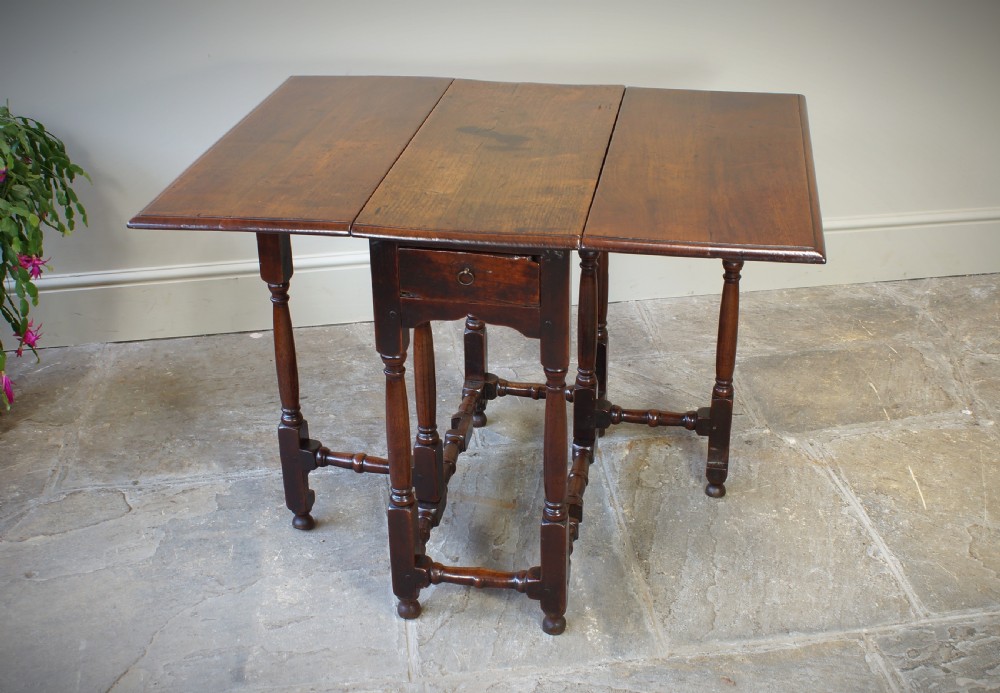 An antique late 17th-century walnut gateleg table featuring turned legs, stretchers, a single frieze drawer, and two hinged drop leaves. View XII