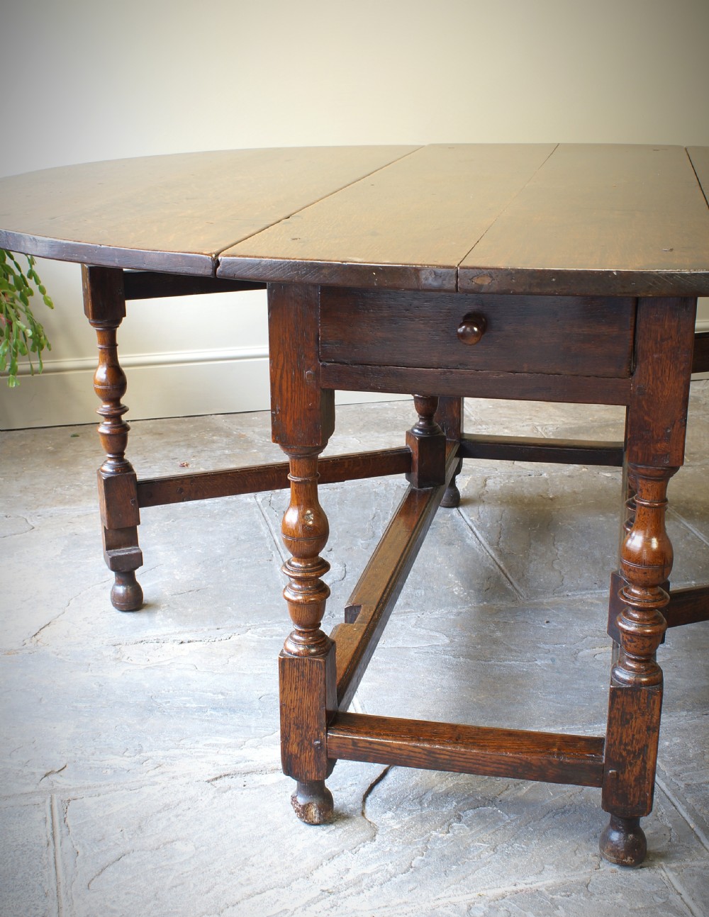 A large 17th-century oak gateleg table featuring an oval drop-leaf top, baluster-turned legs, sturdy box stretchers, and a end drawer. View V