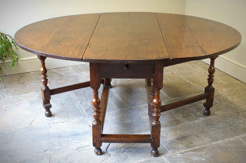 A large 17th-century oak gateleg table featuring an oval drop-leaf top, baluster-turned legs, sturdy box stretchers, and a end drawer.