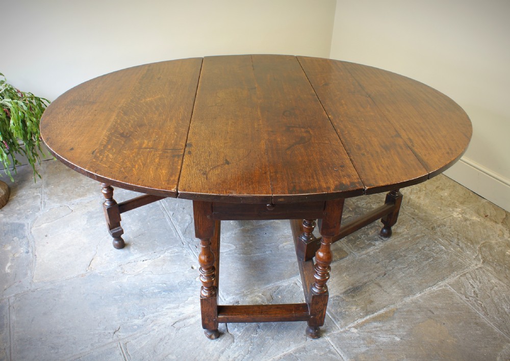 A large 17th-century oak gateleg table featuring an oval drop-leaf top, baluster-turned legs, sturdy box stretchers, and a end drawer. View VI
