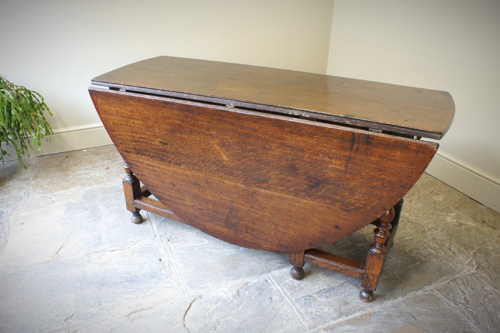 A large 17th-century oak gateleg table featuring an oval drop-leaf top, baluster-turned legs, sturdy box stretchers, and a end drawer. View X