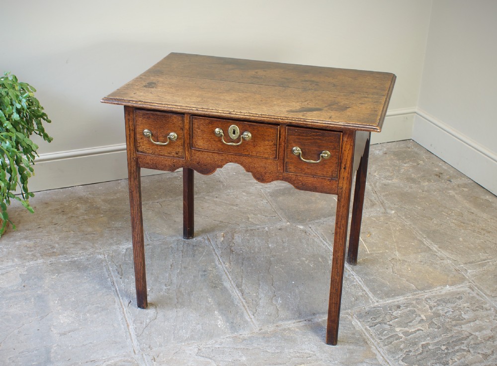 A George III oak lowboy side table featuring three drawers with brass swan-neck handles, a shaped apron, and four square legs. View III