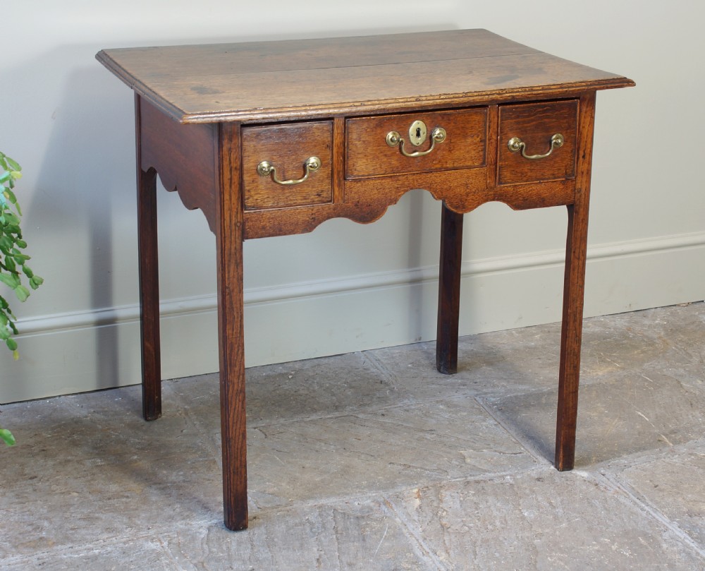 A George III oak lowboy side table featuring three drawers with brass swan-neck handles, a shaped apron, and four square legs. View VIII
