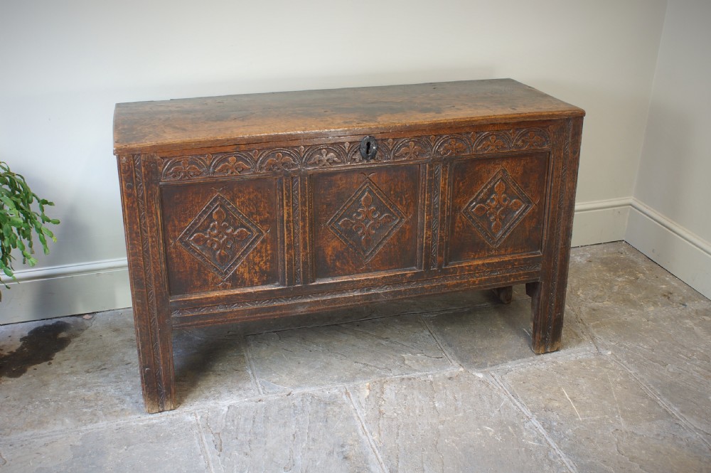 An early 17th-century oak coffer featuring three carved panels with lozenge motifs, an upper carved frieze, and an iron escutcheon. View IX