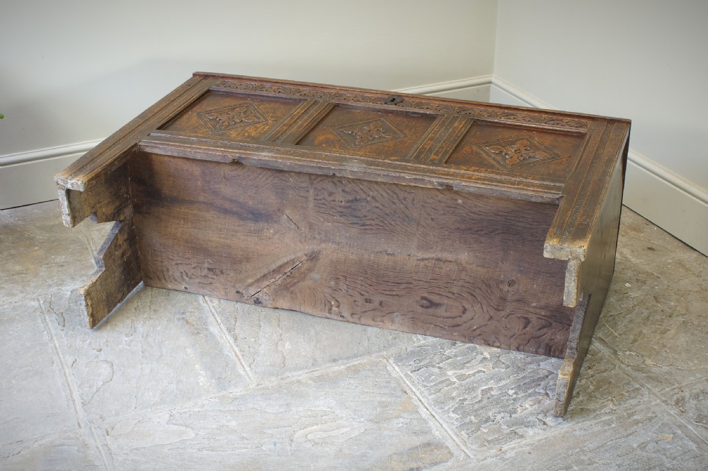 An early 17th-century oak coffer featuring three carved panels with lozenge motifs, an upper carved frieze, and an iron escutcheon. View V