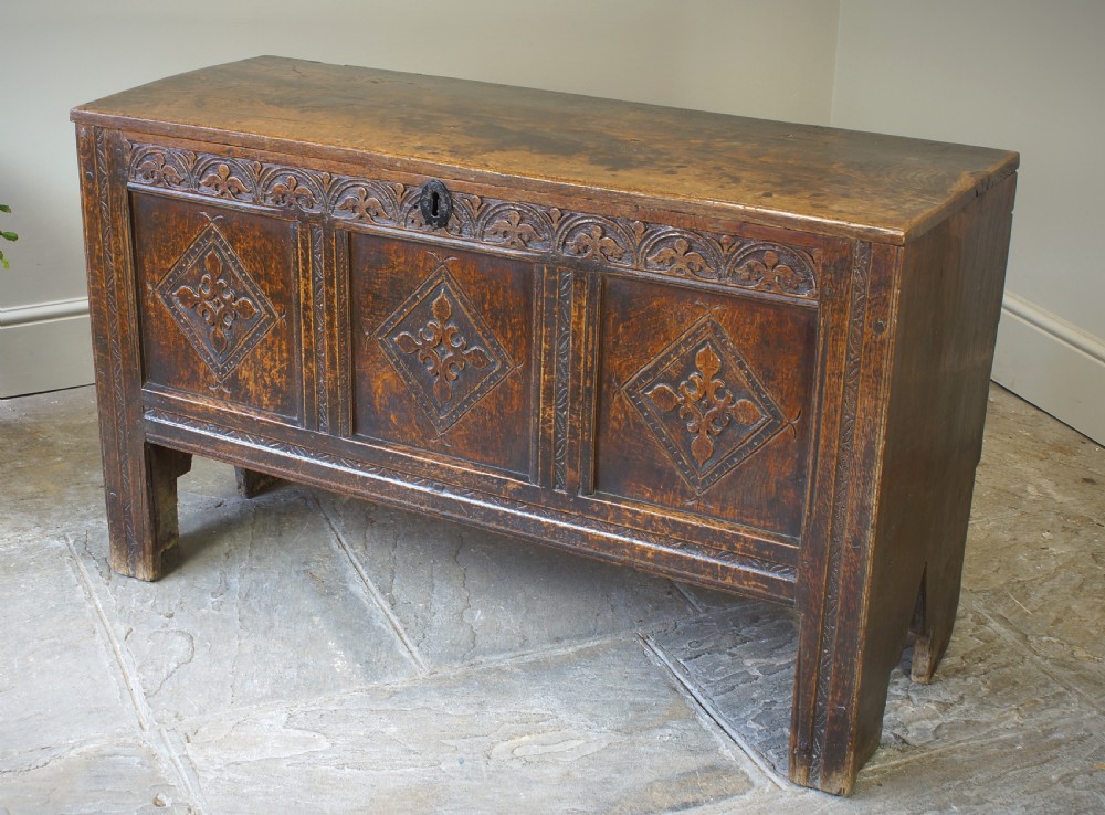 An early 17th-century oak coffer featuring three carved panels with lozenge motifs, an upper carved frieze, and an iron escutcheon. View VI
