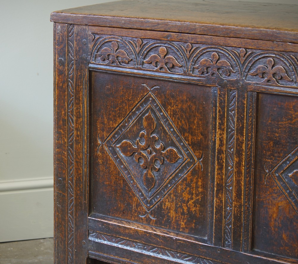 An early 17th-century oak coffer featuring three carved panels with lozenge motifs, an upper carved frieze, and an iron escutcheon. View VIII