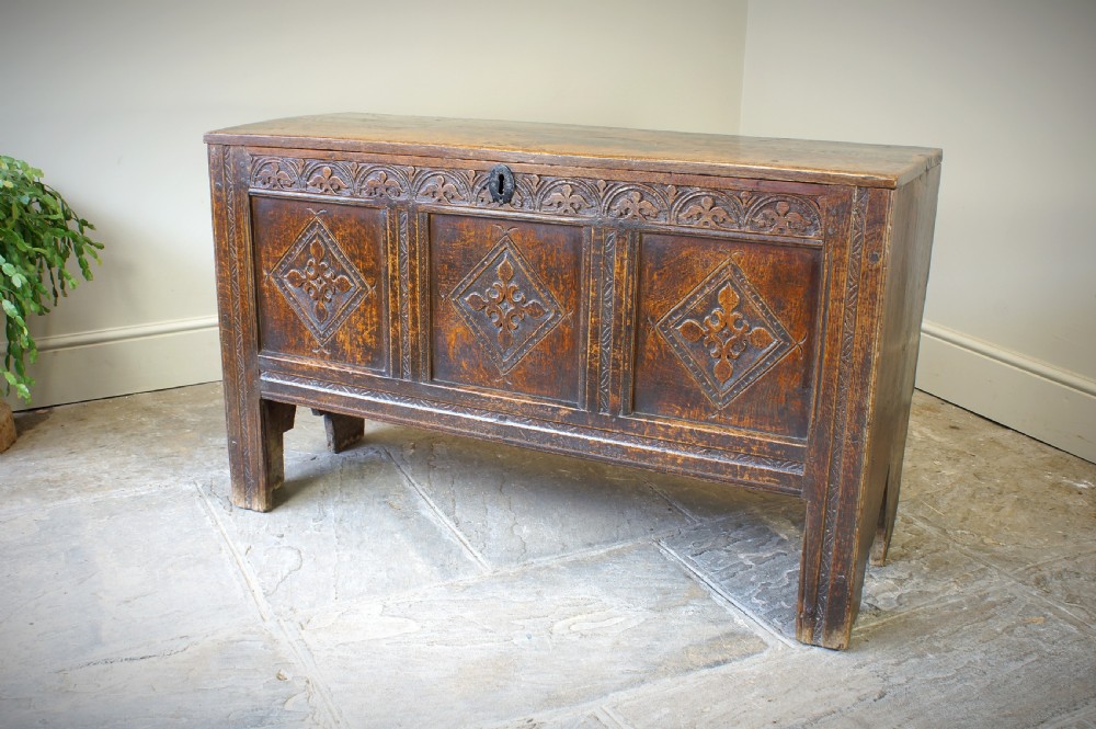 An early 17th-century oak coffer featuring three carved panels with lozenge motifs, an upper carved frieze, and an iron escutcheon.