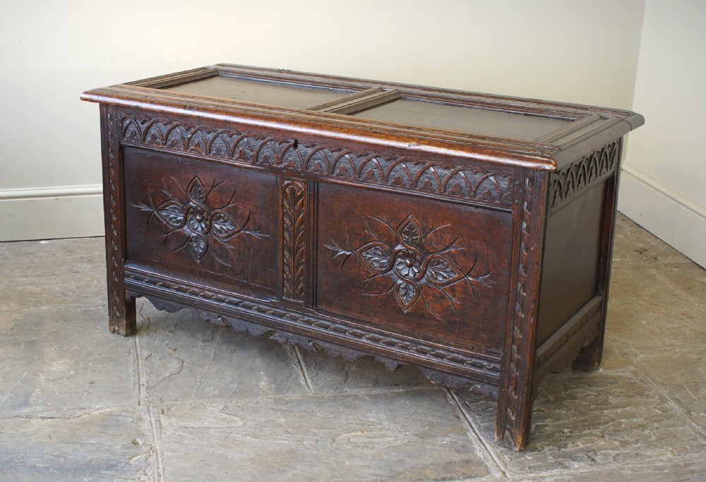 A 17th-century dark oak coffer featuring carved floral panel decoration, a lunette frieze, and a twin-panelled hinged lid.