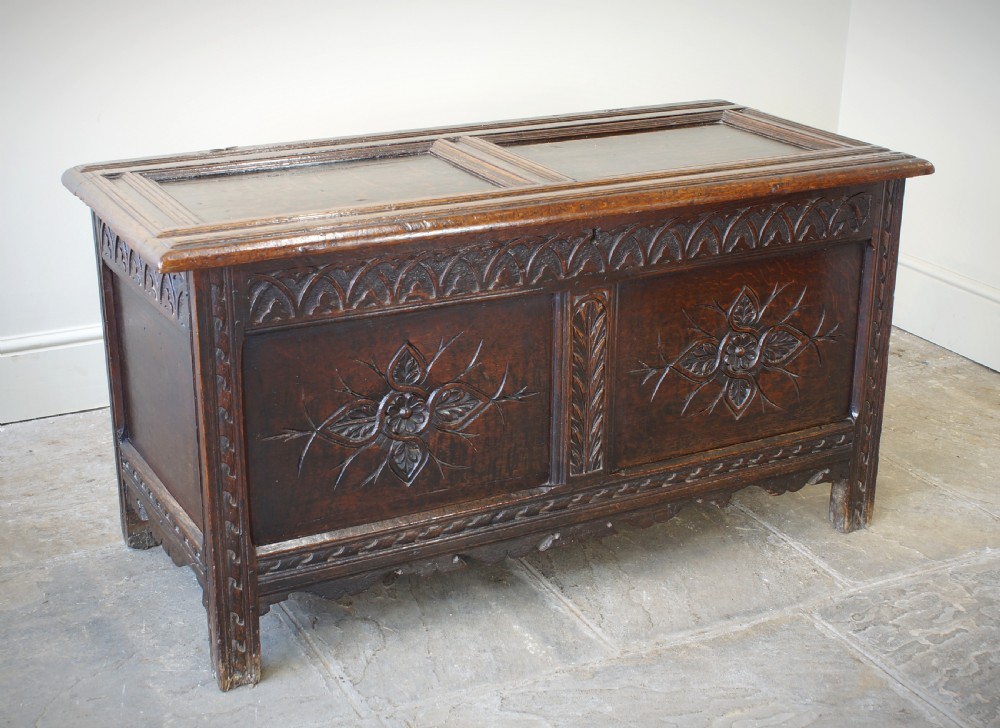 A 17th-century dark oak coffer featuring carved floral panel decoration, a lunette frieze, and a twin-panelled hinged lid. View V