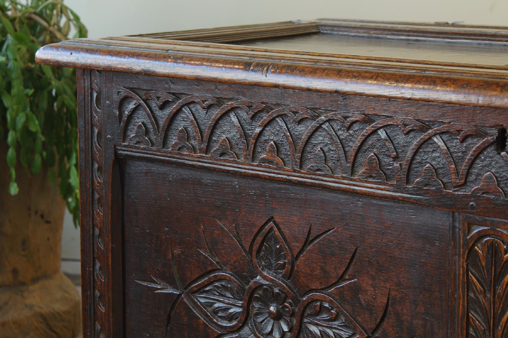 A 17th-century dark oak coffer featuring carved floral panel decoration, a lunette frieze, and a twin-panelled hinged lid. View VI