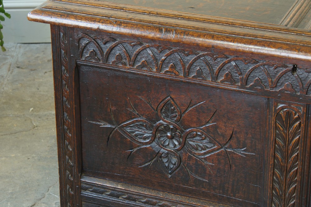 A 17th-century dark oak coffer featuring carved floral panel decoration, a lunette frieze, and a twin-panelled hinged lid. View VIII