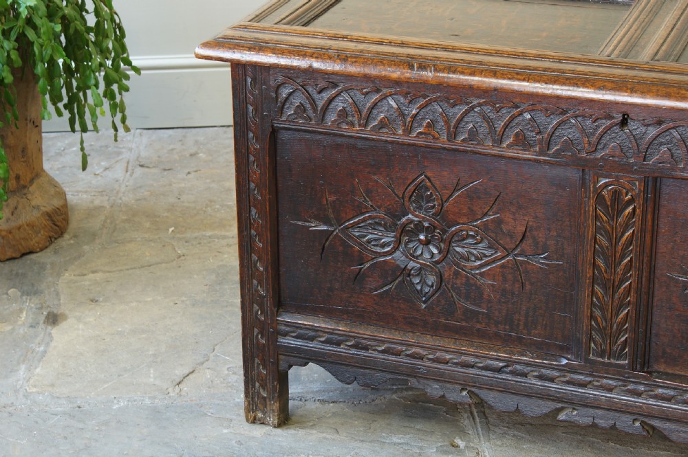 A 17th-century dark oak coffer featuring carved floral panel decoration, a lunette frieze, and a twin-panelled hinged lid. View IX