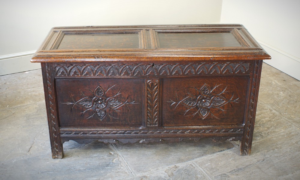 A 17th-century dark oak coffer featuring carved floral panel decoration, a lunette frieze, and a twin-panelled hinged lid. View X