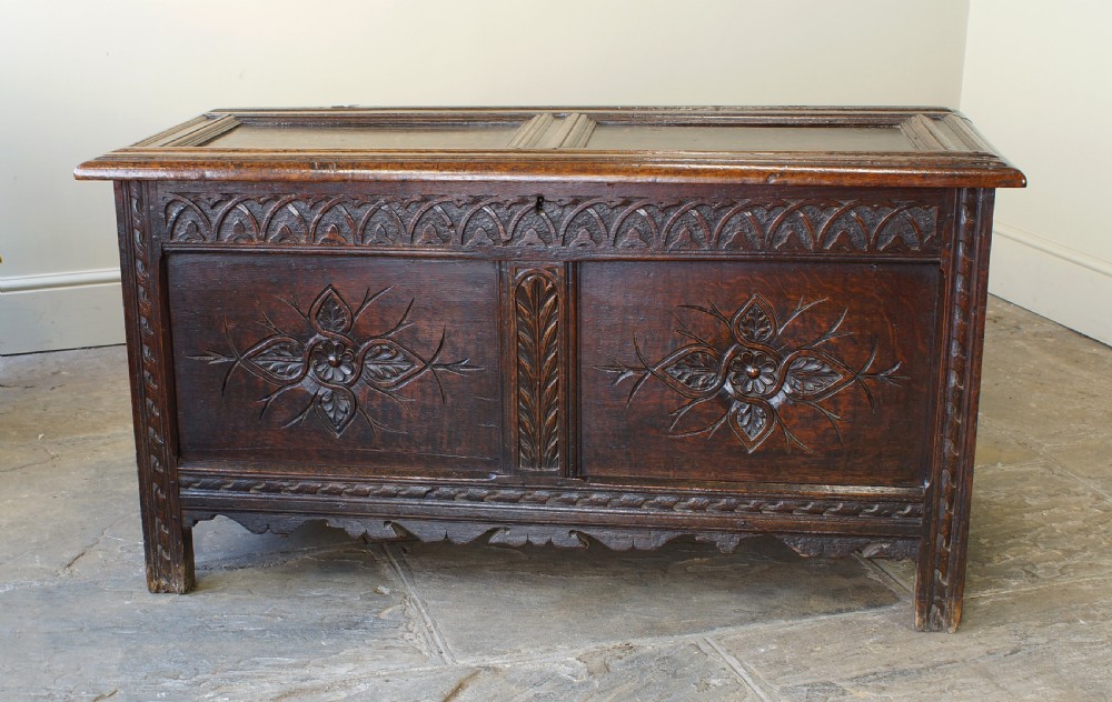 A 17th-century dark oak coffer featuring carved floral panel decoration, a lunette frieze, and a twin-panelled hinged lid. View XI