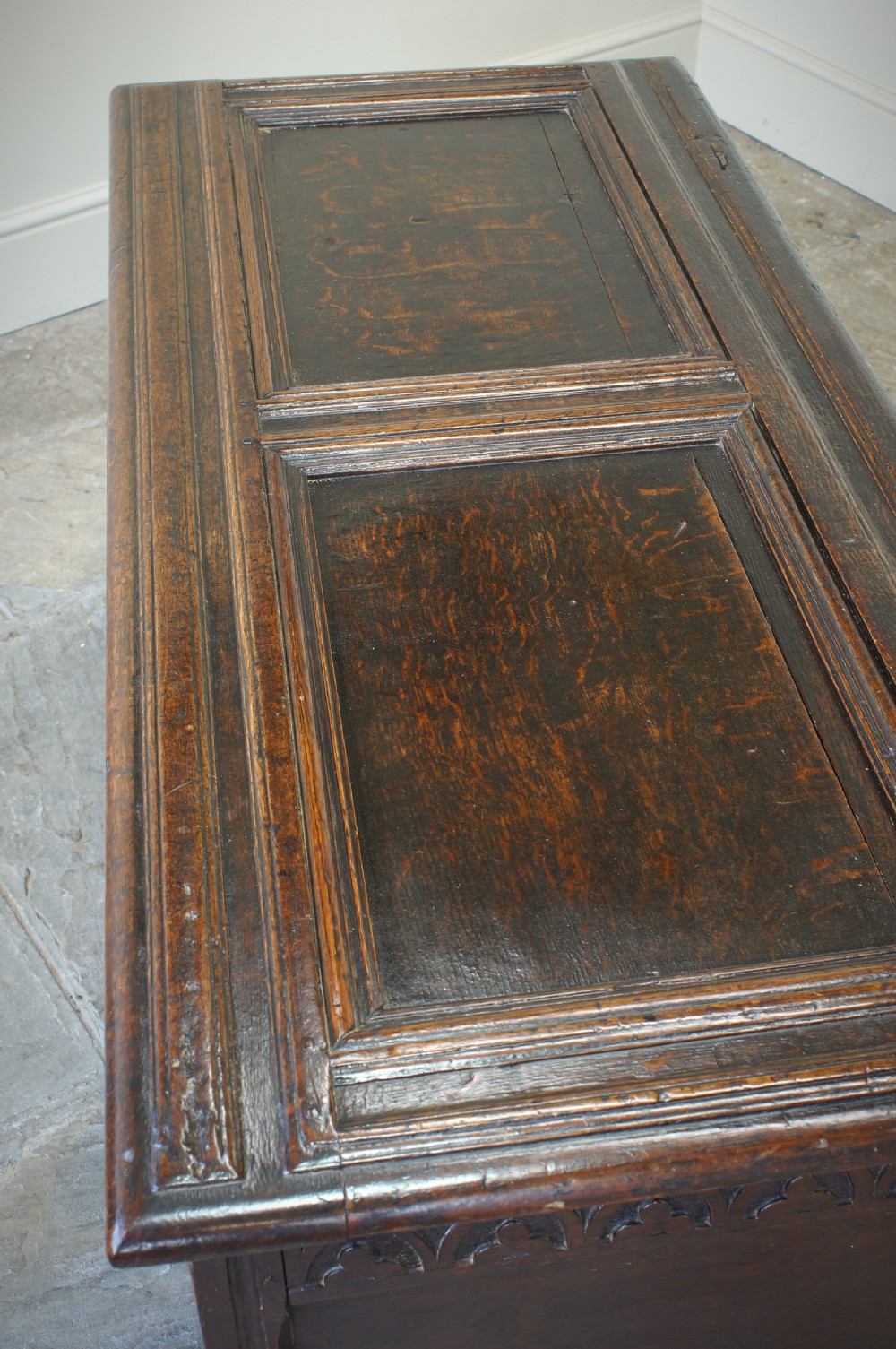 A 17th-century dark oak coffer featuring carved floral panel decoration, a lunette frieze, and a twin-panelled hinged lid. View XII