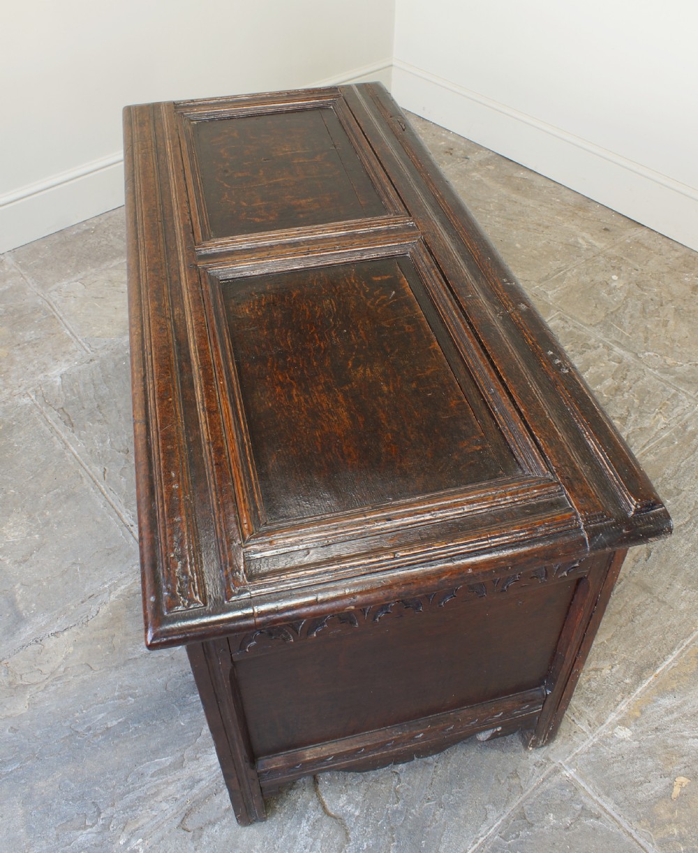 A 17th-century dark oak coffer featuring carved floral panel decoration, a lunette frieze, and a twin-panelled hinged lid. View XIII