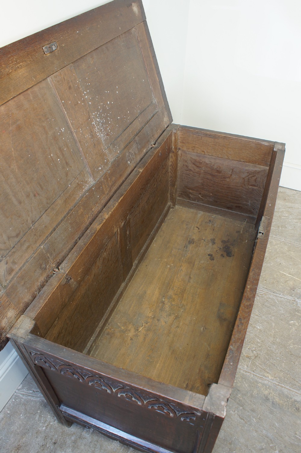 A 17th-century dark oak coffer featuring carved floral panel decoration, a lunette frieze, and a twin-panelled hinged lid. View XV