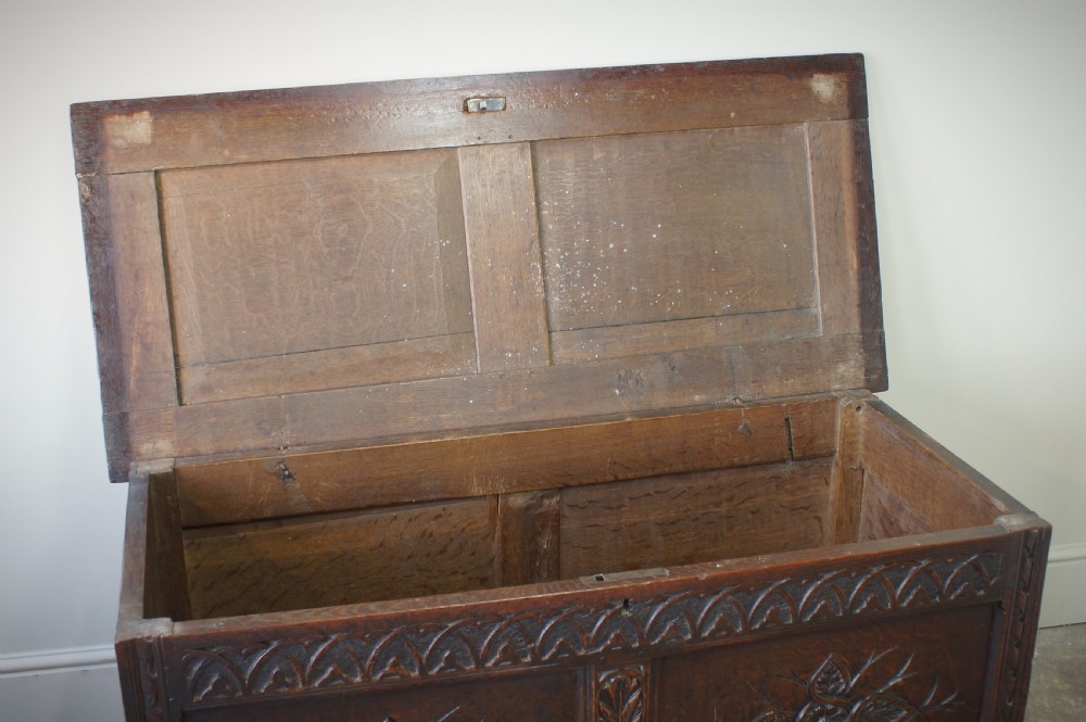 A 17th-century dark oak coffer featuring carved floral panel decoration, a lunette frieze, and a twin-panelled hinged lid. View XVI
