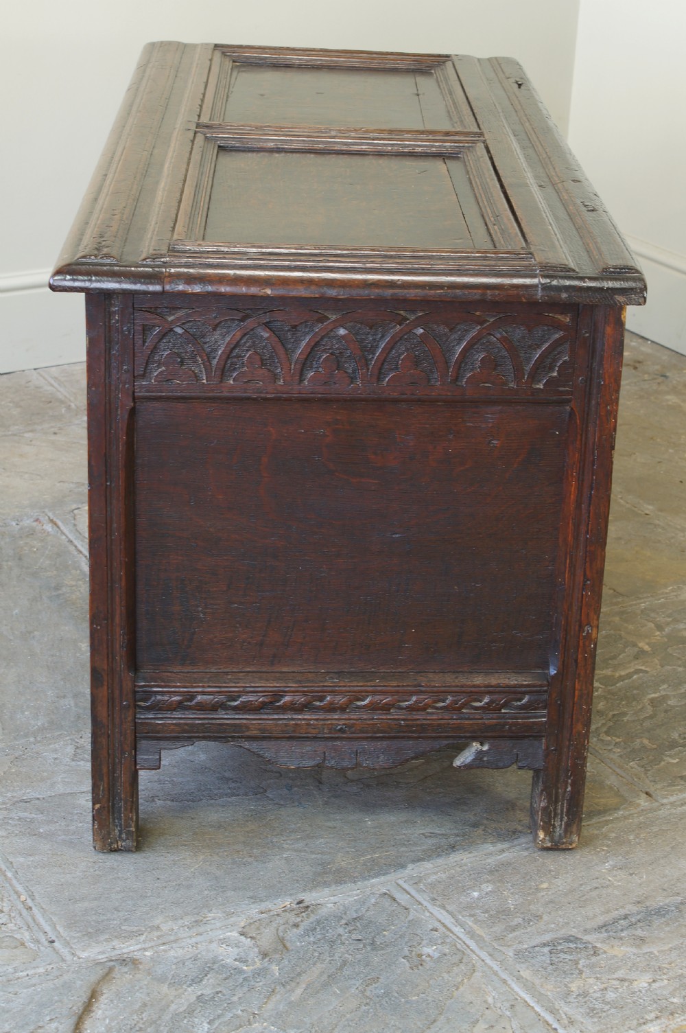A 17th-century dark oak coffer featuring carved floral panel decoration, a lunette frieze, and a twin-panelled hinged lid. View XIX
