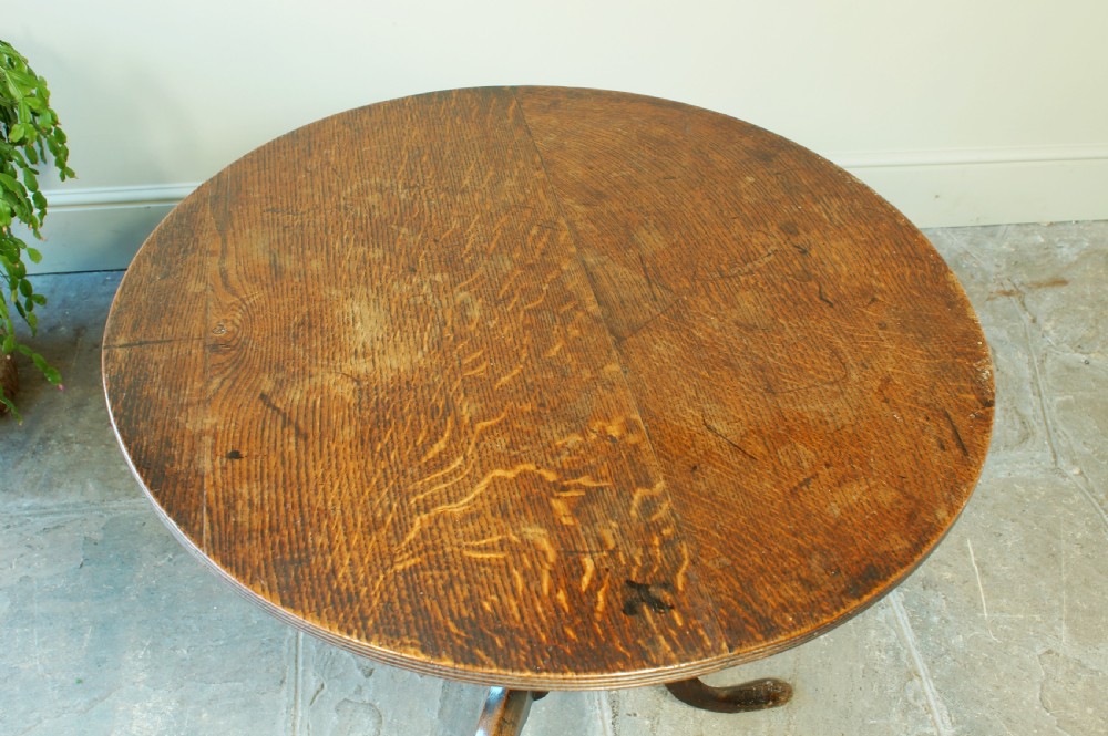 A Georgian oak tilt-top tripod table with a circular top shown in a vertical position, supported by a turned column and three splayed cabriole legs. View III