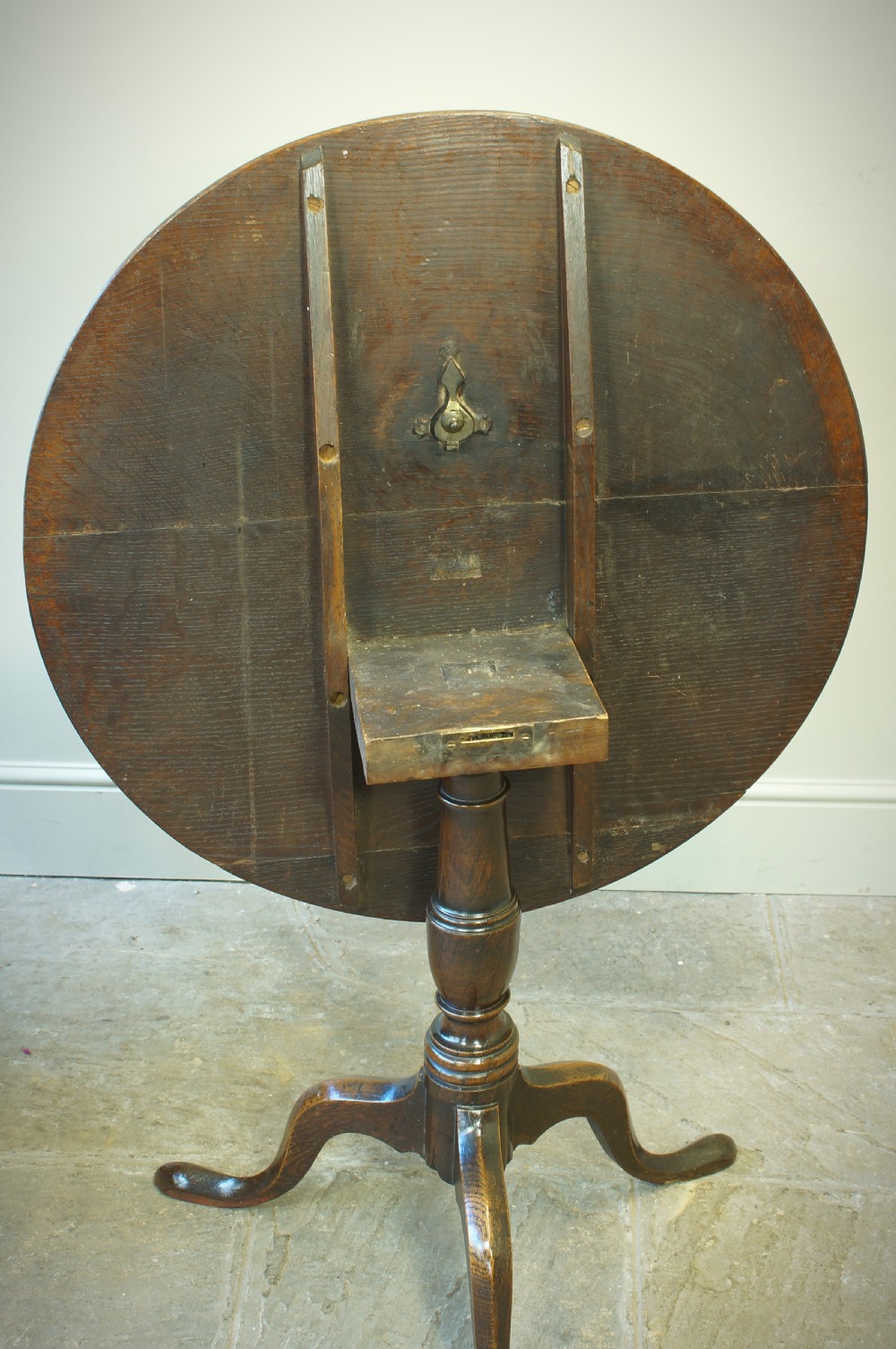 A Georgian oak tilt-top tripod table with a circular top shown in a vertical position, supported by a turned column and three splayed cabriole legs. View V