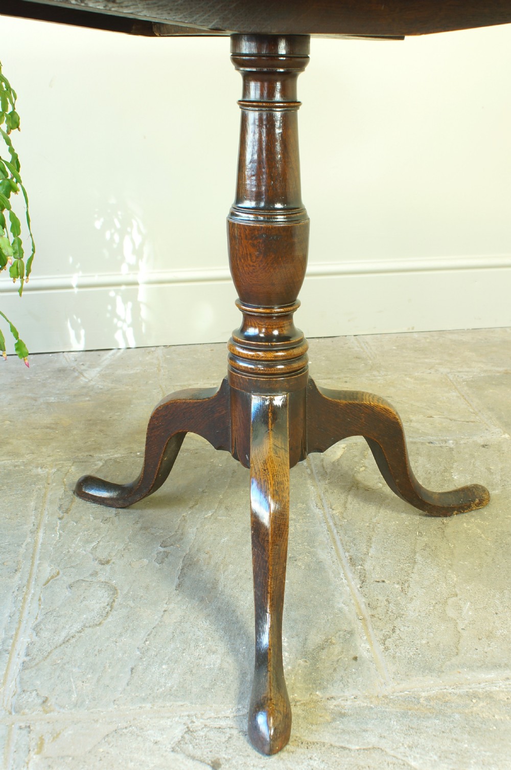 A Georgian oak tilt-top tripod table with a circular top shown in a vertical position, supported by a turned column and three splayed cabriole legs. View VII