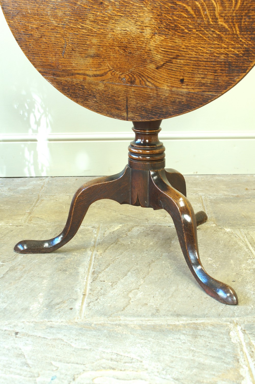 A Georgian oak tilt-top tripod table with a circular top shown in a vertical position, supported by a turned column and three splayed cabriole legs. View VIII