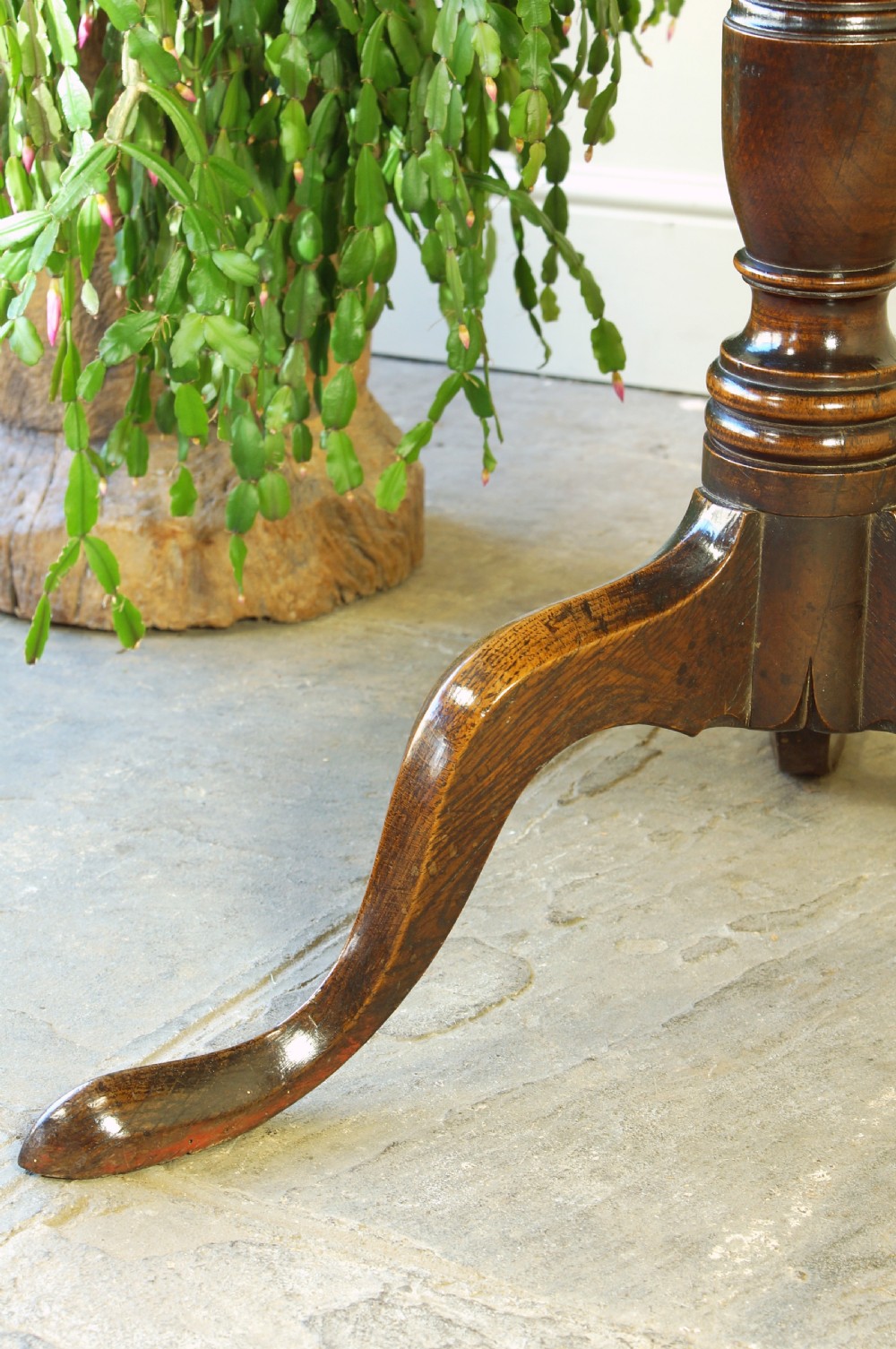 A Georgian oak tilt-top tripod table with a circular top shown in a vertical position, supported by a turned column and three splayed cabriole legs. View X