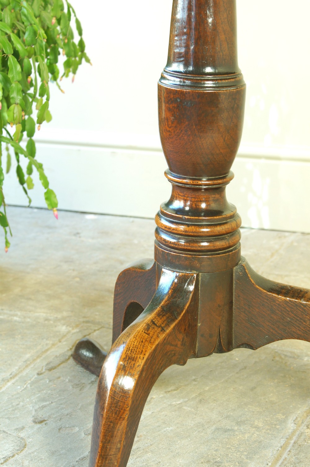 A Georgian oak tilt-top tripod table with a circular top shown in a vertical position, supported by a turned column and three splayed cabriole legs. View XI