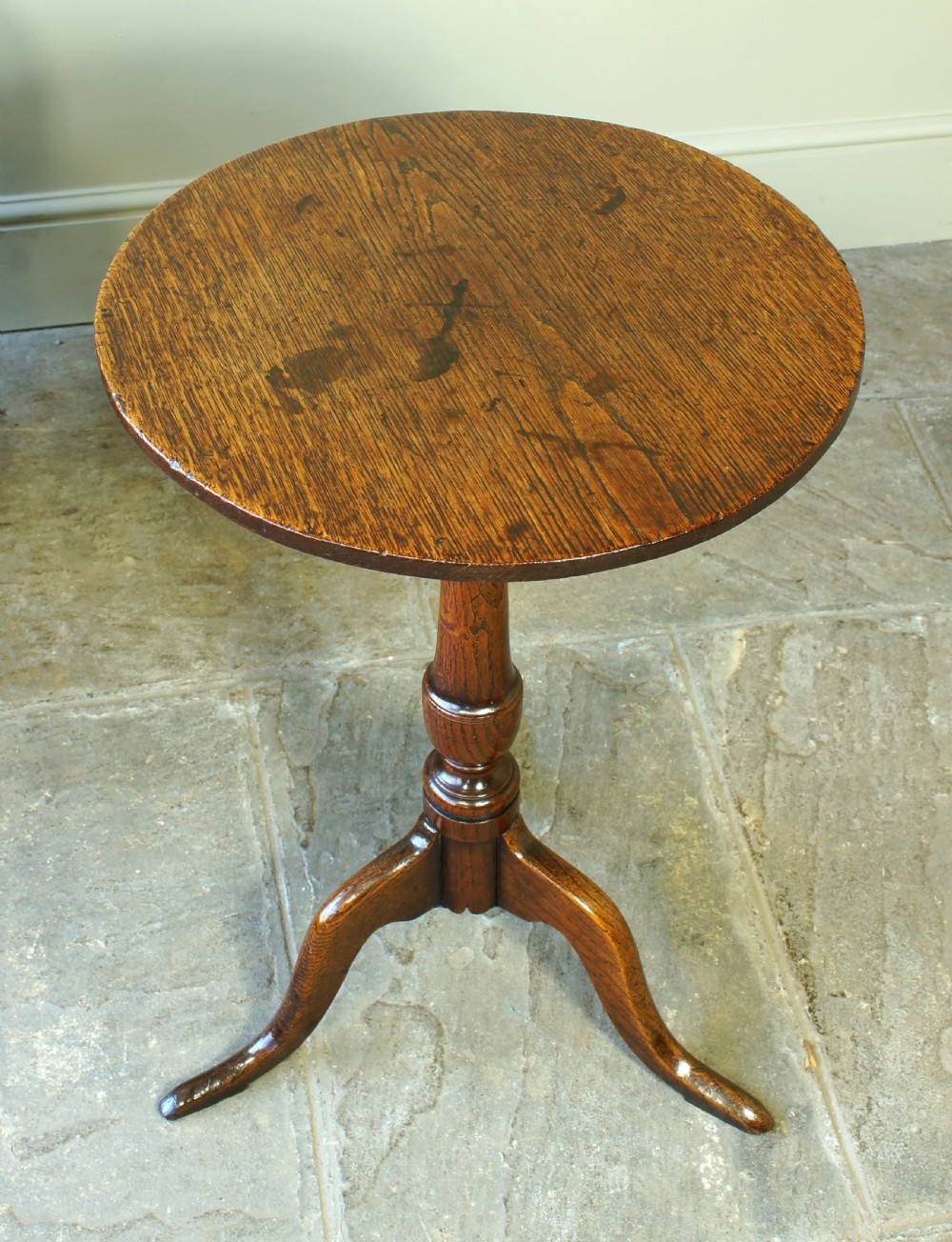 A small circular 18th-century oak tripod table with a turned central column and three curving legs, viewed from above against a neutral background.