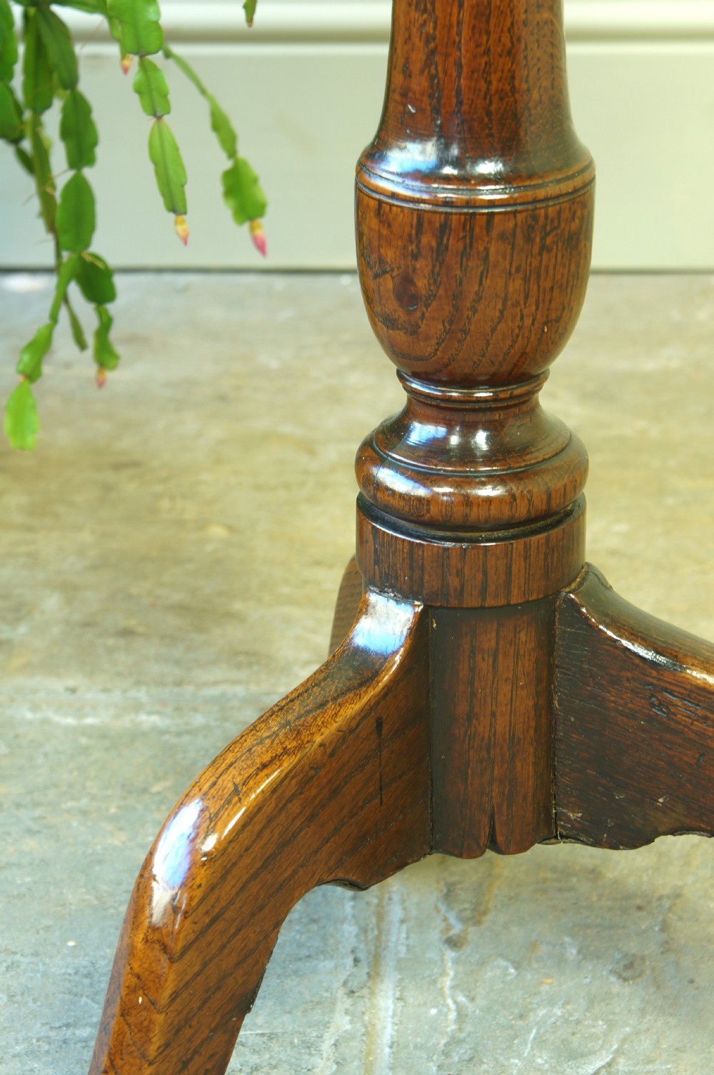 A small circular 18th-century oak tripod table with a turned central column and three curving legs, viewed from above against a neutral background. View VII
