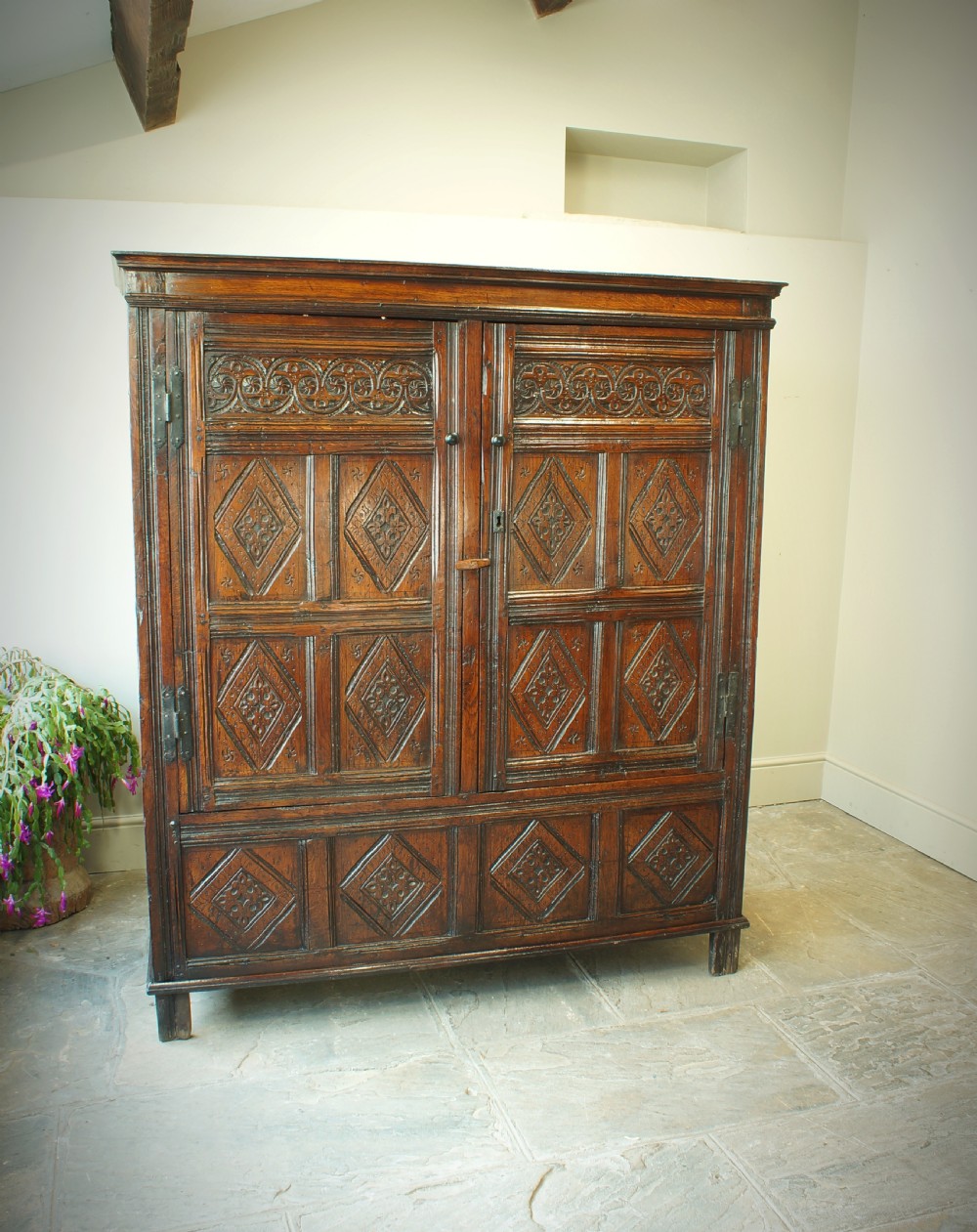 A dark brown seventeenth-century carved oak press cupboard featuring symmetrical panel doors and geometric detailing. View II