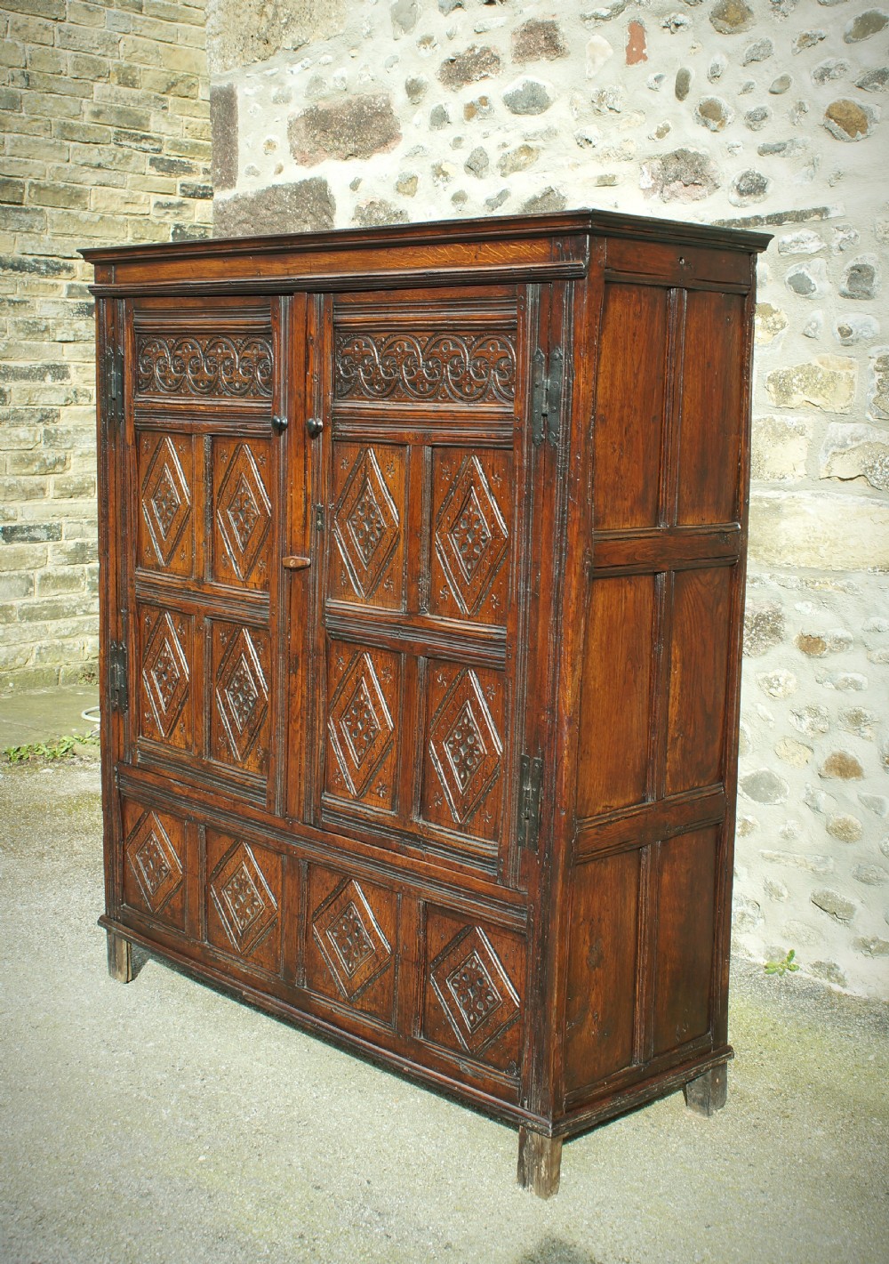 A dark brown seventeenth-century carved oak press cupboard featuring symmetrical panel doors and geometric detailing. View III