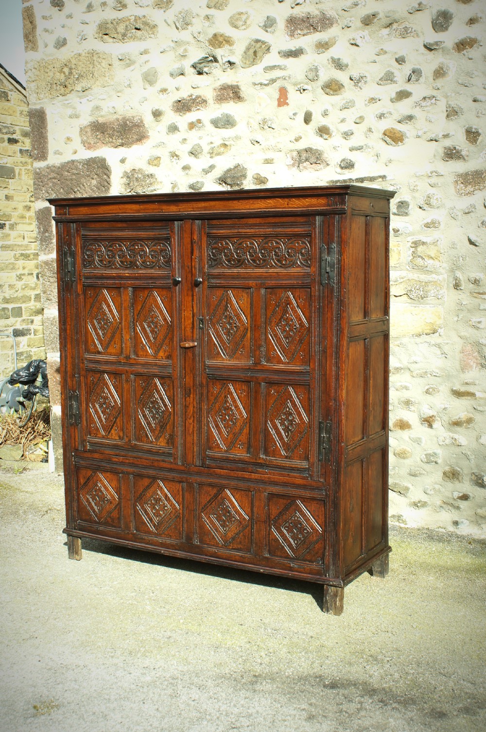A dark brown seventeenth-century carved oak press cupboard featuring symmetrical panel doors and geometric detailing.