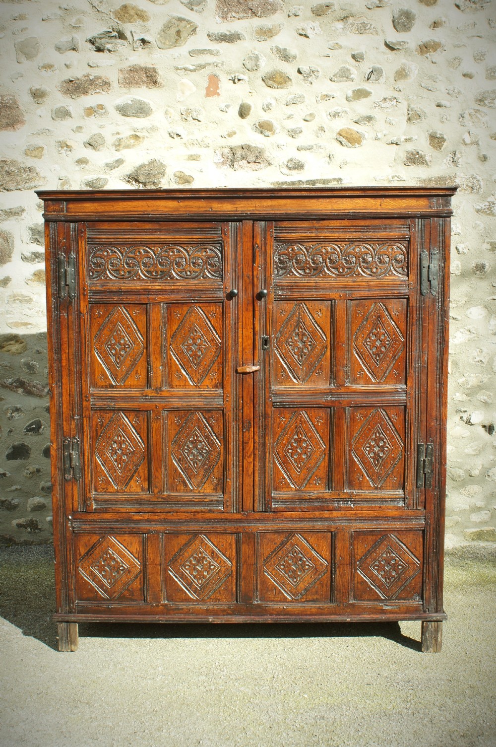 A dark brown seventeenth-century carved oak press cupboard featuring symmetrical panel doors and geometric detailing. View IV