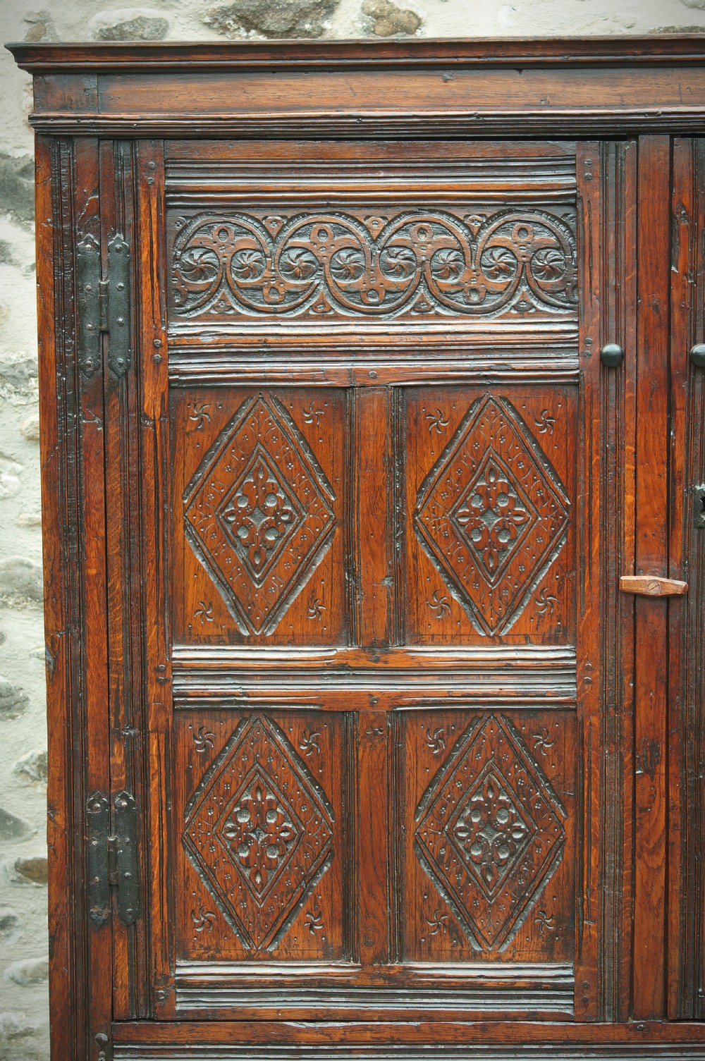 A dark brown seventeenth-century carved oak press cupboard featuring symmetrical panel doors and geometric detailing. View V