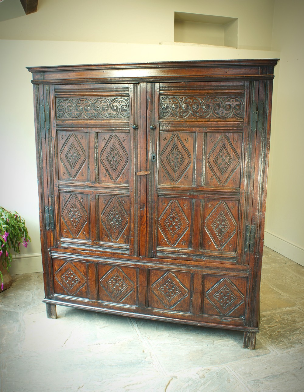 A dark brown seventeenth-century carved oak press cupboard featuring symmetrical panel doors and geometric detailing. View VIII